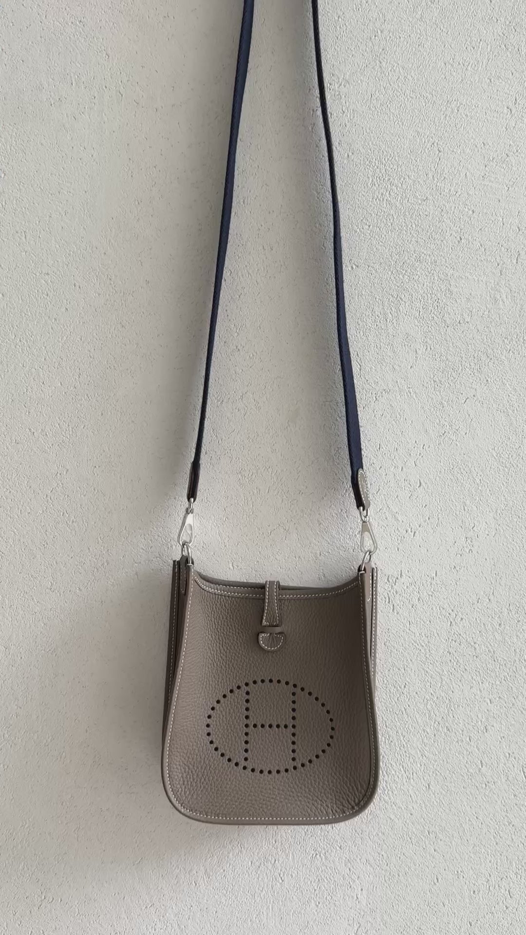 Hermès Evelyne 16 Amazone in der Farbe Etoupe mit dem charakteristischen perforierten „H“-Logo und einem kontrastierenden Schulterriemen in der Farbe bleu/indigo.
